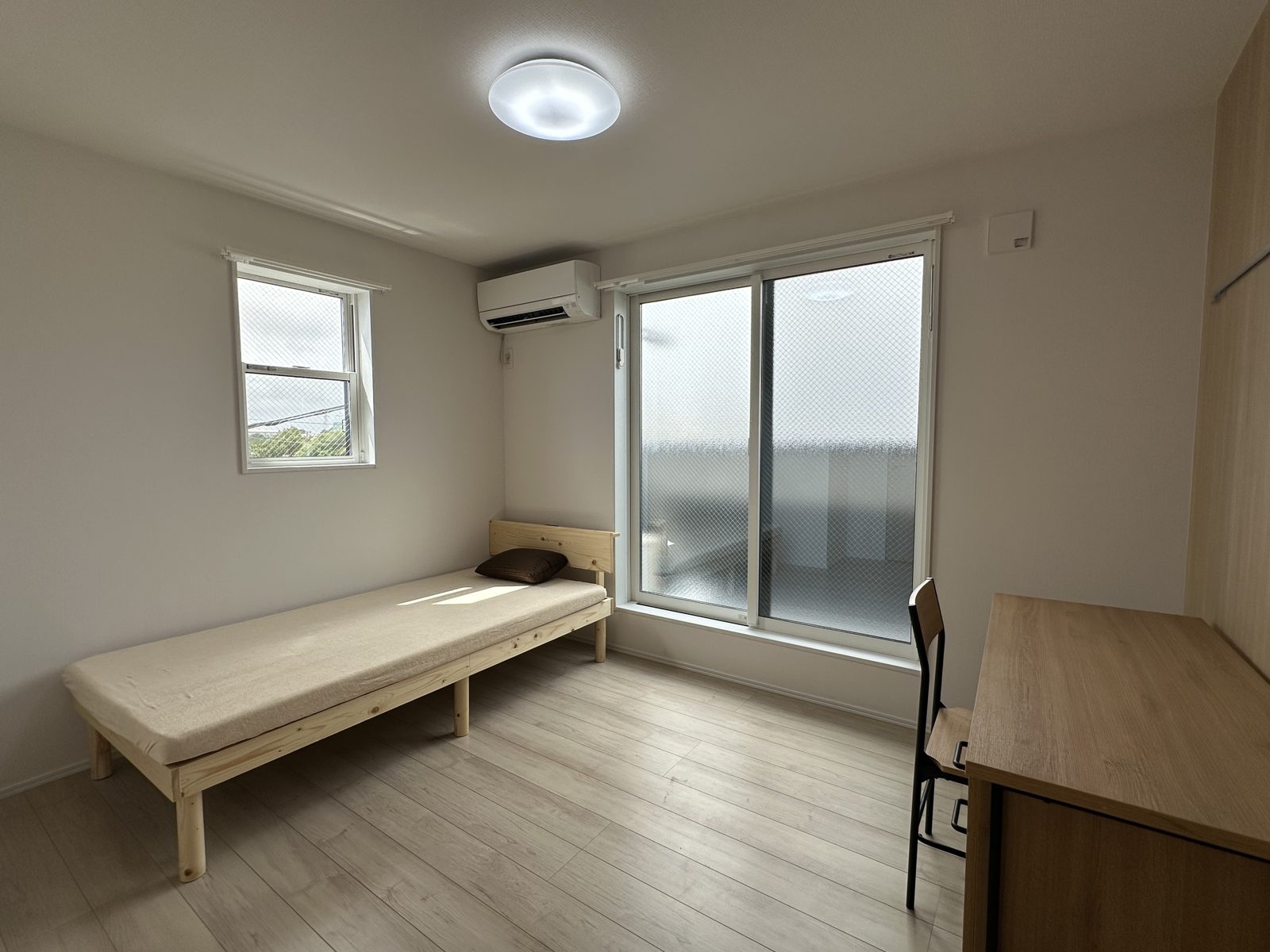Furnished studio main room with bed, desk, chair and air conditioner